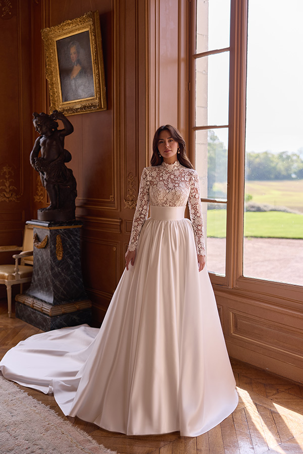 Junge Frau in elegantem weißen Brautkleid mit Spitzenoberteil steht am Fenster