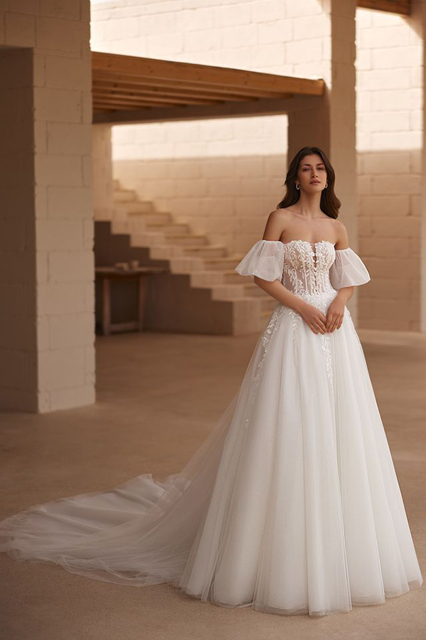 Junge Frau mit elegantem Gesichtsausdruck in weißem Brautkleid mit Spitze und langen Schleier