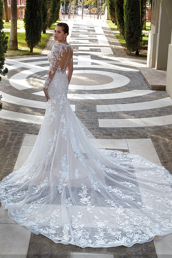 Eine Frau mit hellem Teint schaut ernst über die Schulter und trägt ein weißes Spitzenkleid mit langer Schleppe