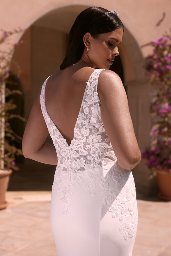 Eine Frau mit dunklen Haaren trägt ein elegantes weißes Spitzenkleid und schaut ernst