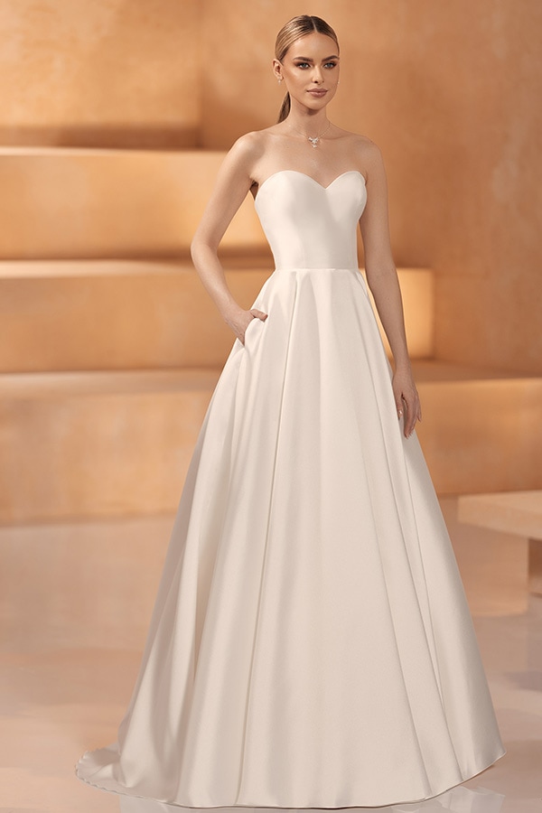 Junge Frau mit neutralem Ausdruck trägt ein elegantes cremefarbenes, schulterfreies Kleid