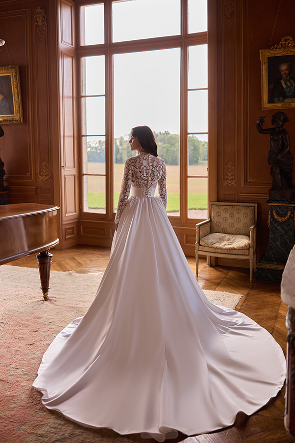 Eine Frau im eleganten weißen Brautkleid blickt ruhig aus großen Fensterfronten