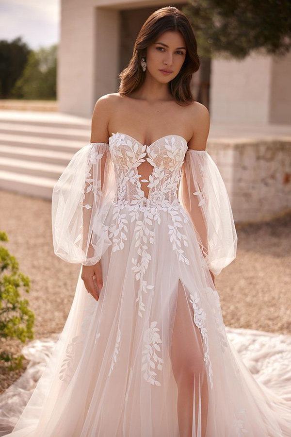 Junge Frau mit sanftem Lächeln im cremefarbenen Brautkleid mit Spitzendetails und Puffärmeln