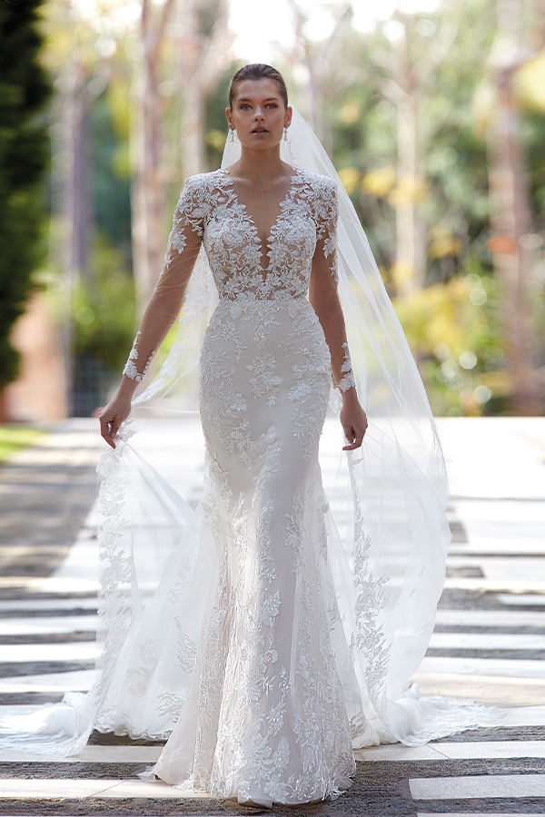 Junge Frau im eleganten weißen Spitzenkleid steht nachdenklich mit langem Schleier draußen