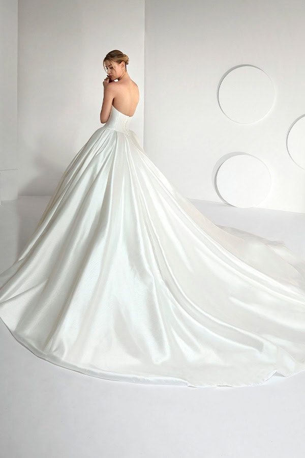 Eine blonde Frau im eleganten weißen Brautkleid blickt lächelnd über die Schulter