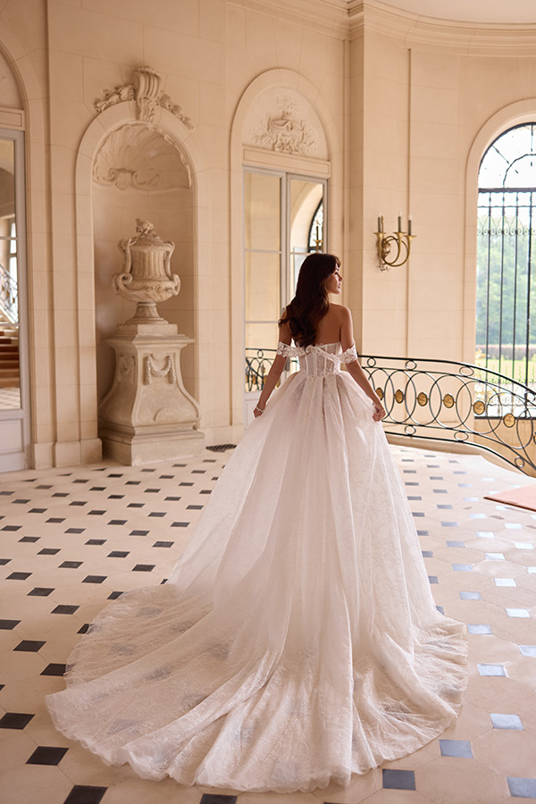 Eine braunhaarige Frau in weißem Brautkleid steht elegant in einem hellen Saal