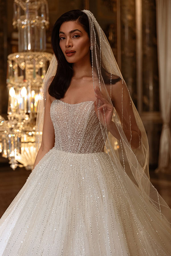 Junge Frau mit sanftem Lächeln trägt ein glitzerndes Brautkleid und langen Schleier