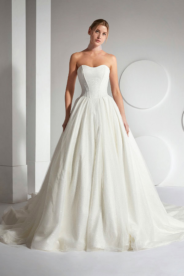 Eine blonde Frau mit ernstem Blick trägt ein elegantes weißes trägerloses Brautkleid