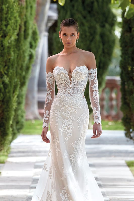 Eine brünette Frau mit ernstem Blick trägt ein cremefarbenes Spitzenkleid im Garten