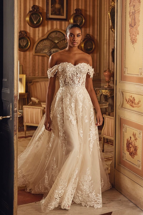 Eine Frau mit ernstem Blick trägt ein elegantes cremefarbenes Spitzenkleid im Salon