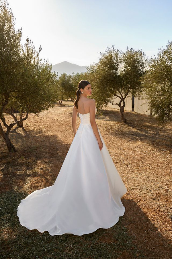 Eine Frau mit ernstem Blick steht im weißen Brautkleid auf einem Feldweg
