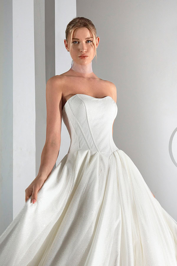 Junge Frau mit ernstem Blick trägt elegantes weißes schulterfreies Brautkleid