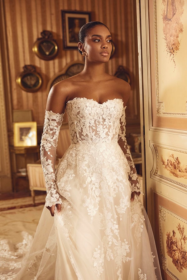 Junge Frau mit elegantem Spitzenkleid und ruhigem Blick in warmem Zimmer mit Goldtönen