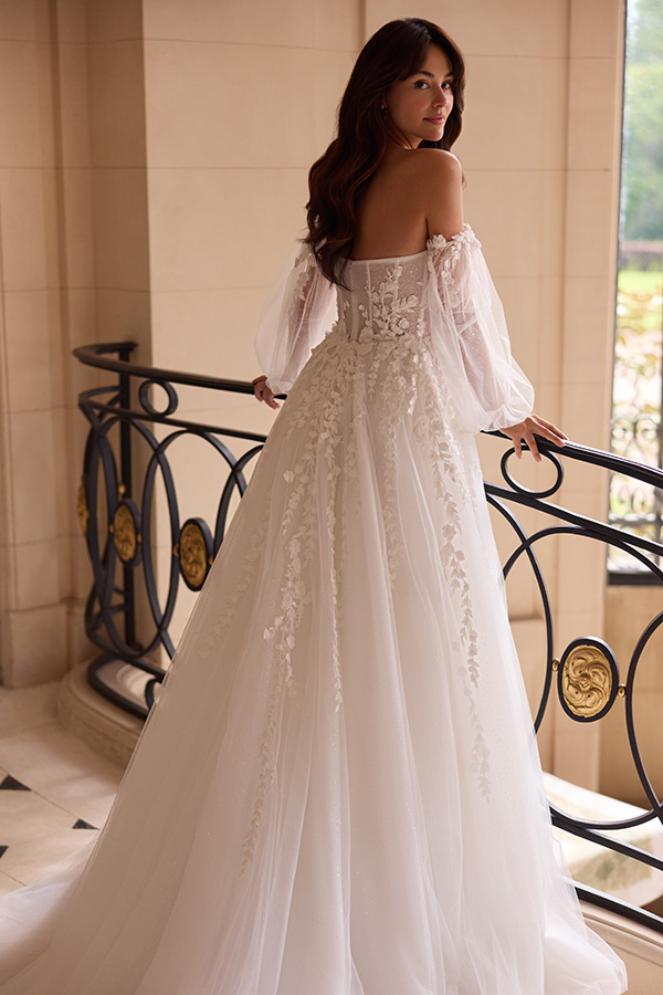 Junge Frau mit langen braunen Haaren trägt ein weißes Brautkleid mit Spitze und blickt lächelnd über die Schulter