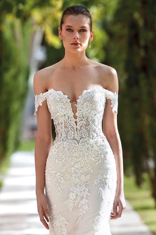 Eine junge Frau mit neutralem Gesichtsausdruck trägt ein elegantes Spitzenkleid in Weiß