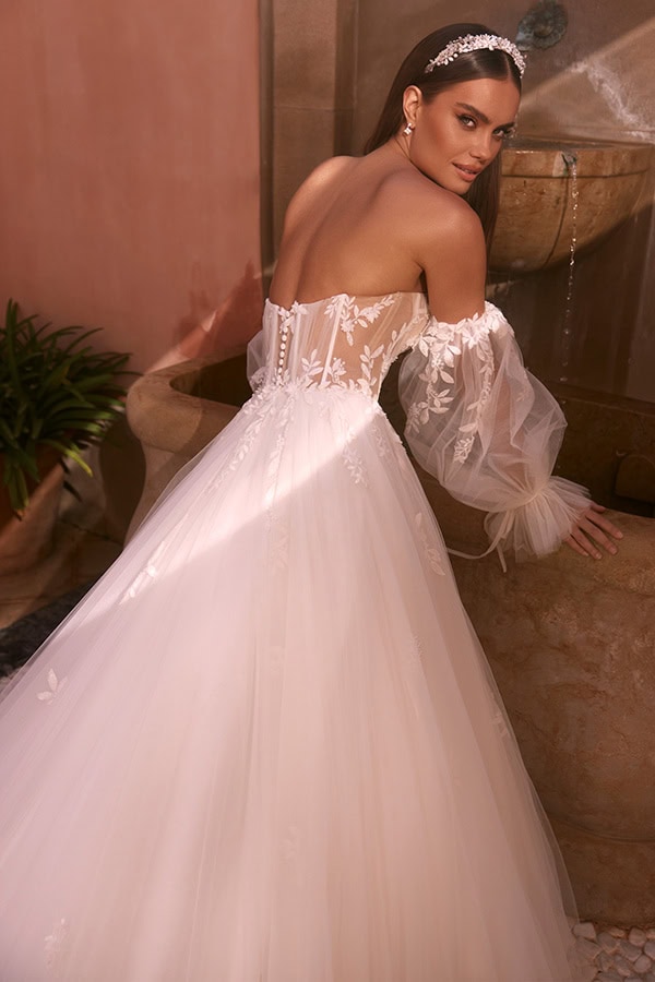 Eine Frau in weißem Brautkleid mit Spitze lächelt leicht und trägt ein Diadem