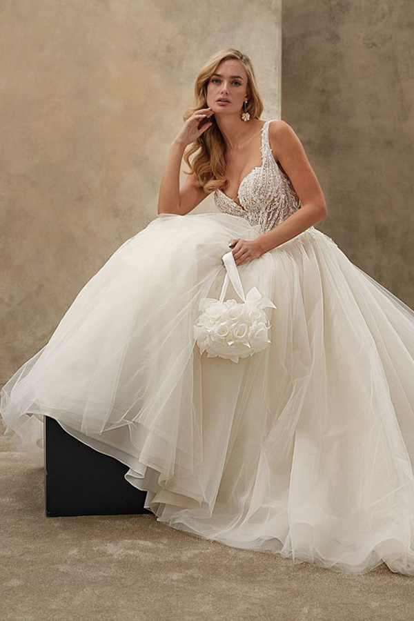 Eine blonde Frau im cremeweißen Brautkleid sitzt entspannt und hält eine Rosenhandtasche