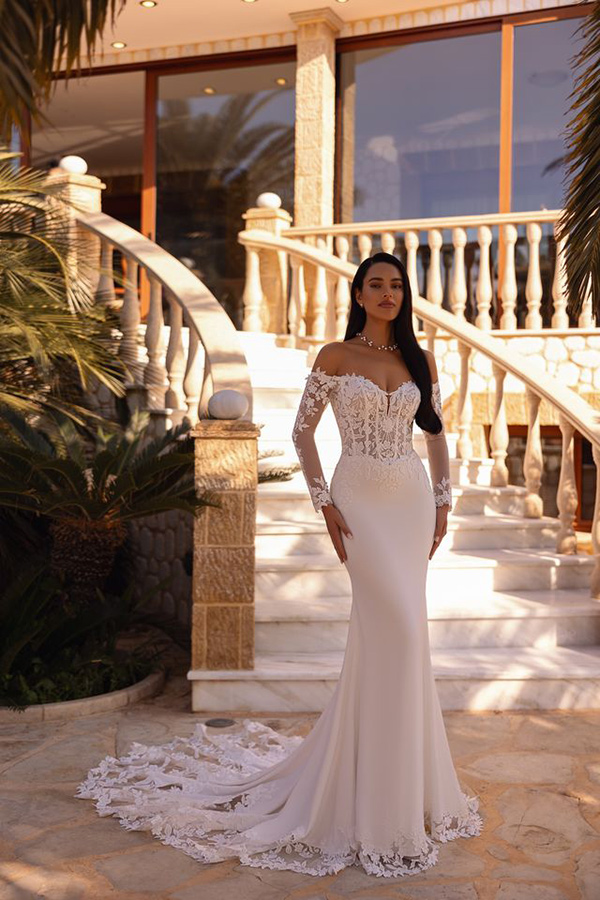 Eine Frau mit langem dunklem Haar trägt ein elegantes weißes Brautkleid und schaut ruhig