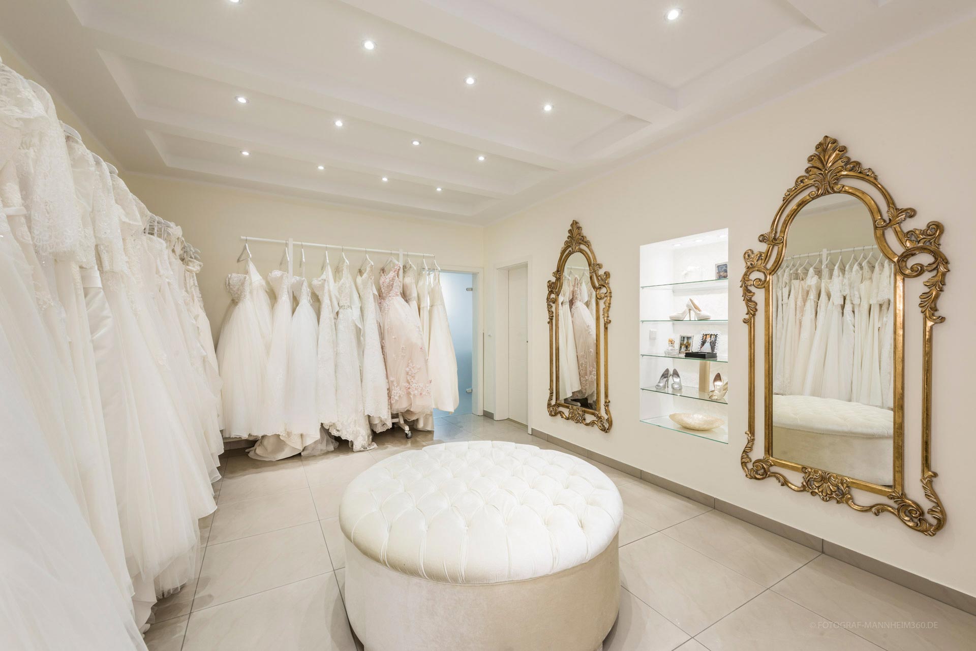 Eleganter Ankleideraum mit weißen Brautkleidern, goldenen Spiegeln und Polsterhocker