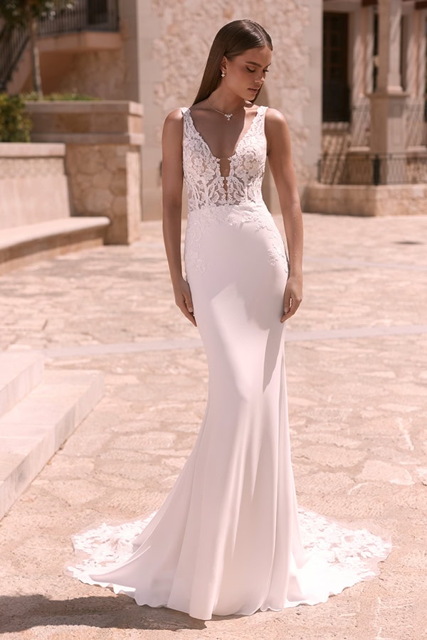 Eine junge Frau mit ernstem Blick trägt ein weißes, elegantes, figurbetontes Brautkleid