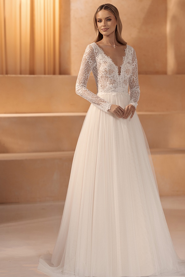 Junge Frau lächelt sanft in weißem Spitzenkleid mit langem Rock und transparenten Ärmeln