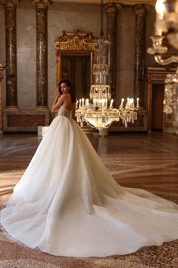 Eine junge Frau in einem weißen Brautkleid steht lächelnd neben einem Kronleuchter