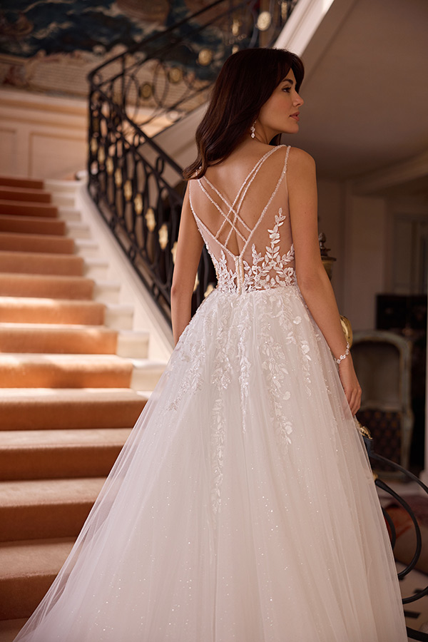 Braunhaarige Frau lächelt leicht in weißem Brautkleid mit Spitzenrücken und zarten Trägern