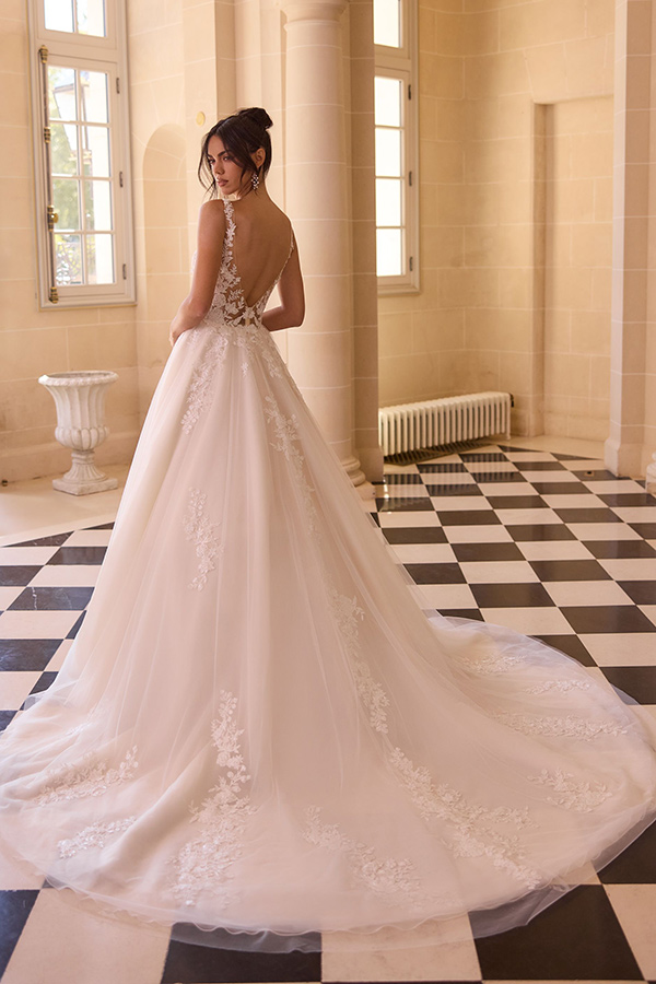 Eine Frau im eleganten weißen Brautkleid steht lächelnd vor großen Fenstern