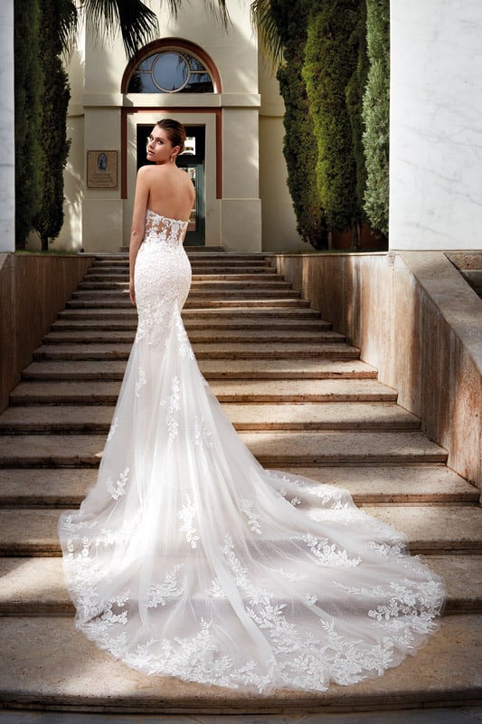 Eine junge Frau mit elegantem Ausdruck trägt ein weißes Spitzenkleid auf einer Treppe