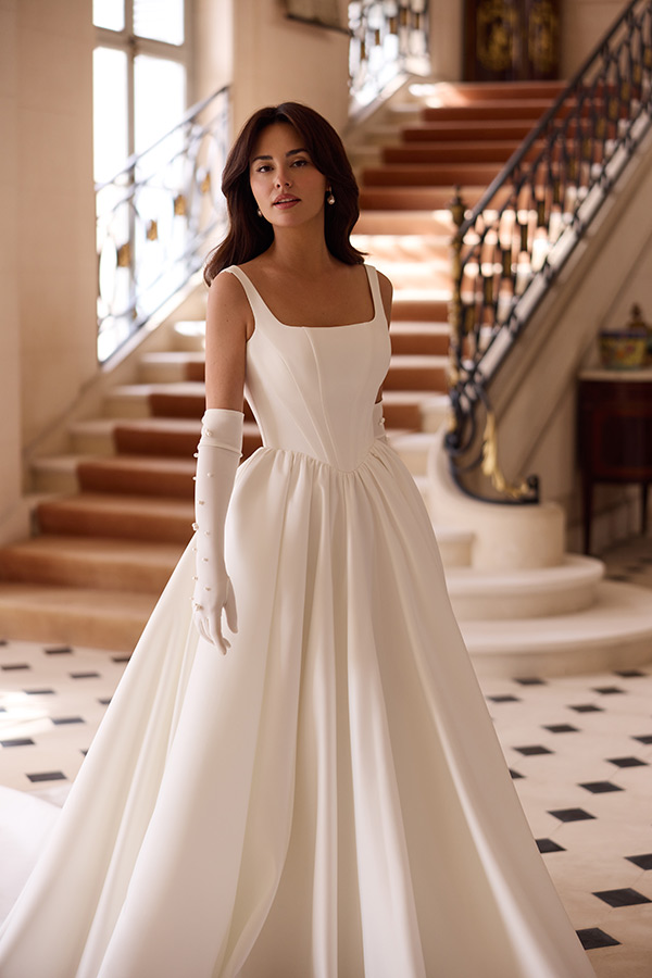 Junge Frau mit elegantem weißen Kleid und Handschuhen steht vor einem Treppenhaus