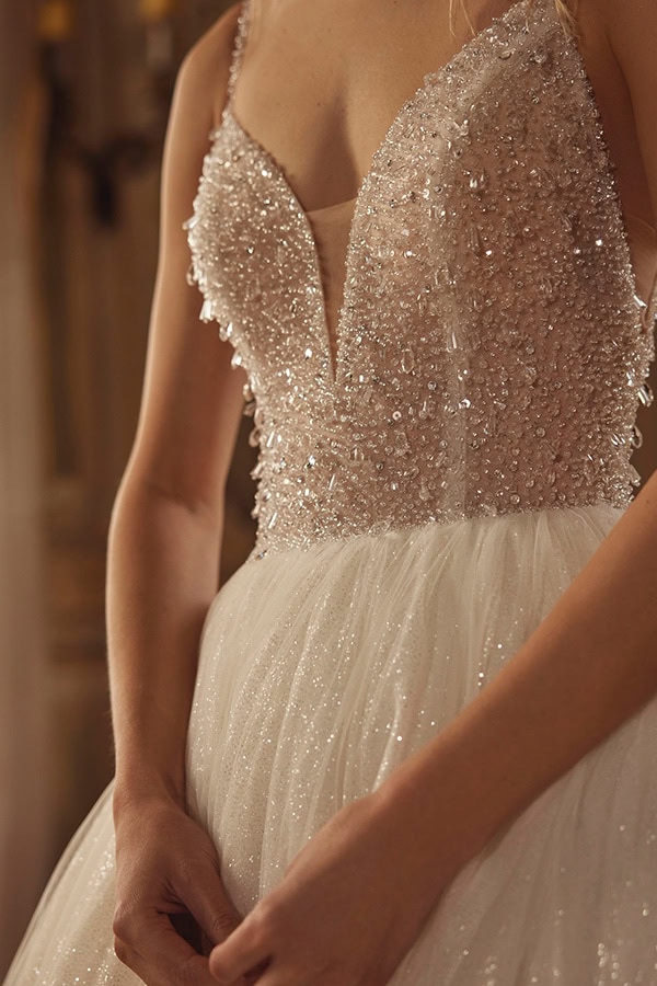 Eine Frau im funkelnden, ärmellosen Brautkleid mit Perlendetails wirkt nachdenklich