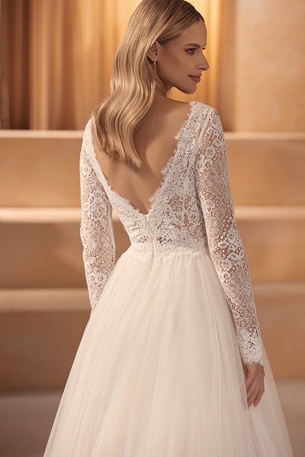 Junge Frau mit langen blonden Haaren trägt lächelnd ein weißes Spitzenbrautkleid