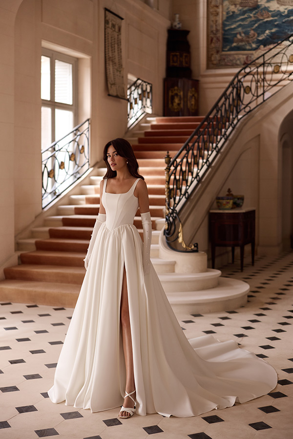 Eine brünette Frau im eleganten cremefarbenen Brautkleid steht vor einer prunkvollen Treppe