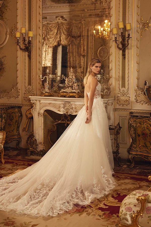 Junge Frau im weißen Brautkleid mit Spitzen am langen Schleier steht elegant im prunkvollen Raum