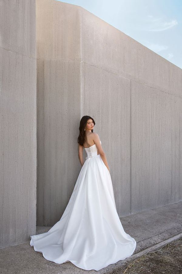 Eine Frau mit braunen Haaren im weißen Brautkleid blickt lächelnd über die Schulter