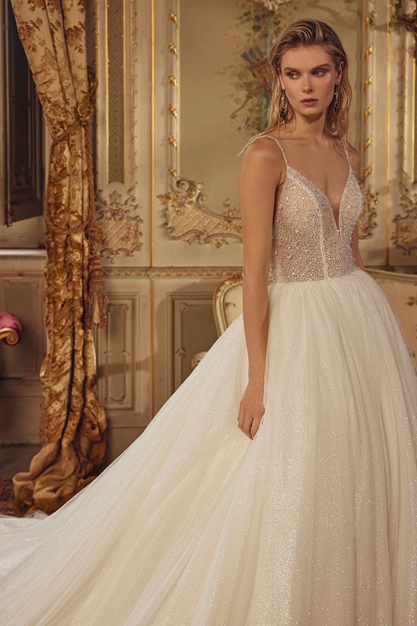 Junge Frau mit ernstem Blick trägt glitzerndes cremeweißes Brautkleid in prunkvollem Raum