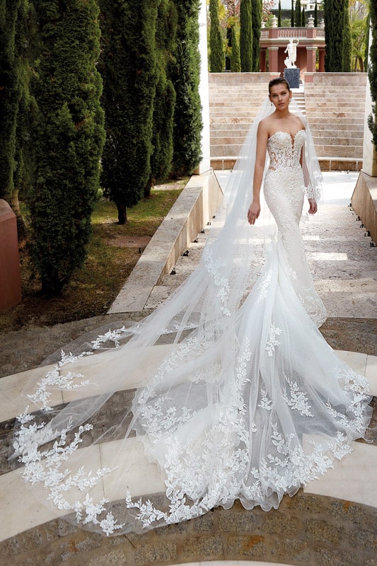 Eine lächelnde Frau in einem eleganten weißen Brautkleid mit langer Spitzen-Schleppe