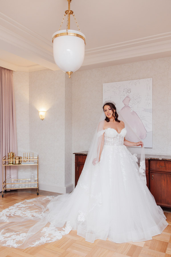 Eine lächelnde Frau im eleganten weißen Brautkleid steht in einem stilvollen Raum