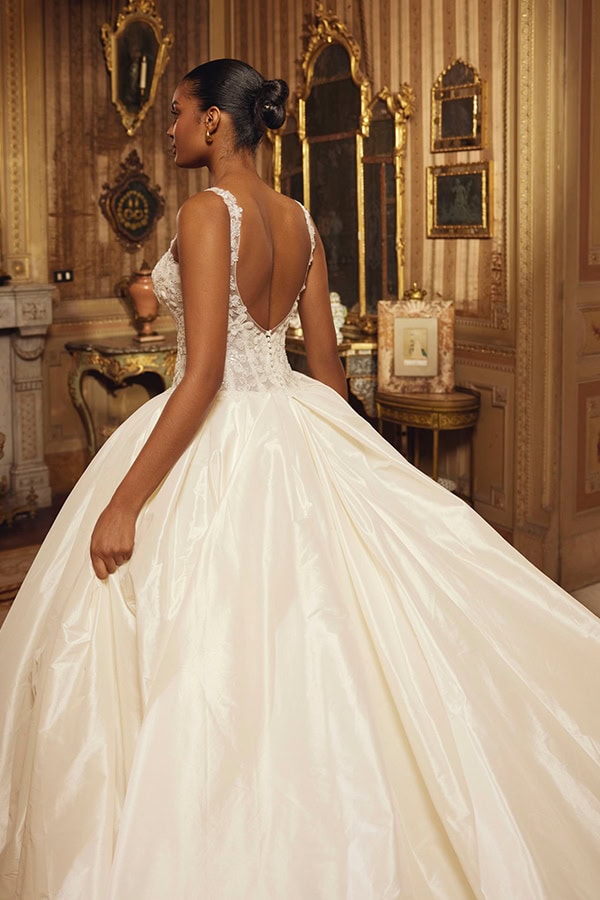 Junge Frau im eleganten, weißen Brautkleid mit Spitze steht vor goldenen Spiegeln