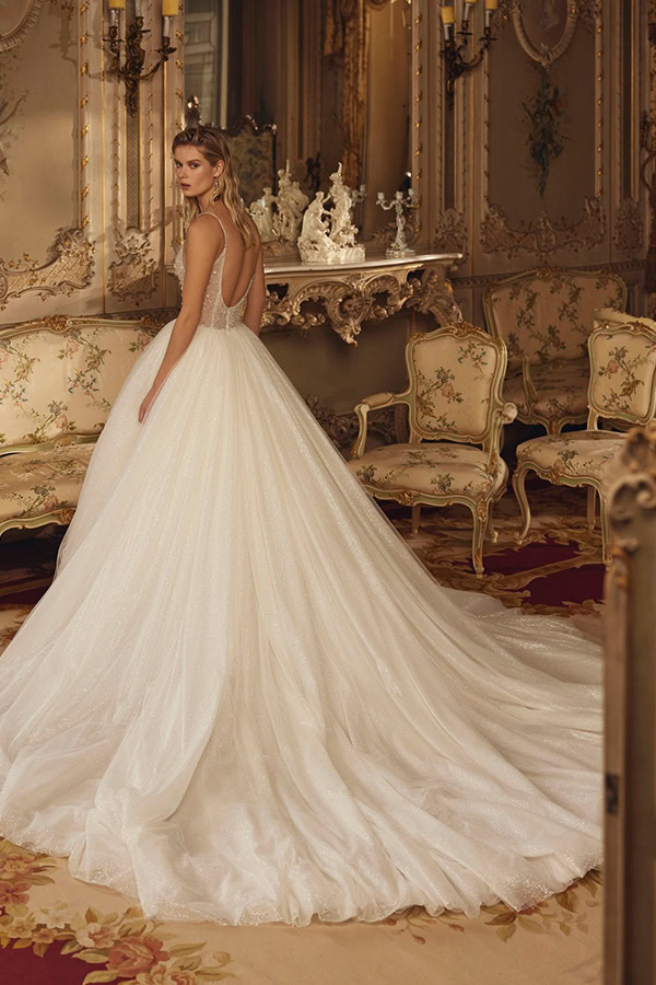 Eine blonde Frau im eleganten weißen Brautkleid blickt ernst über die Schulter