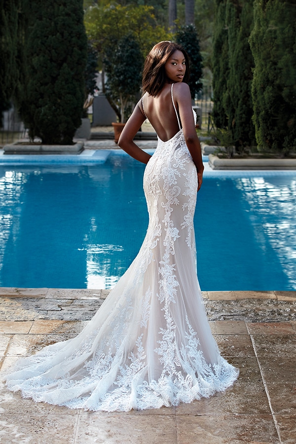 Eine elegant gekleidete Frau steht in einem weißen Spitzenkleid vor einem Pool und blickt zurück