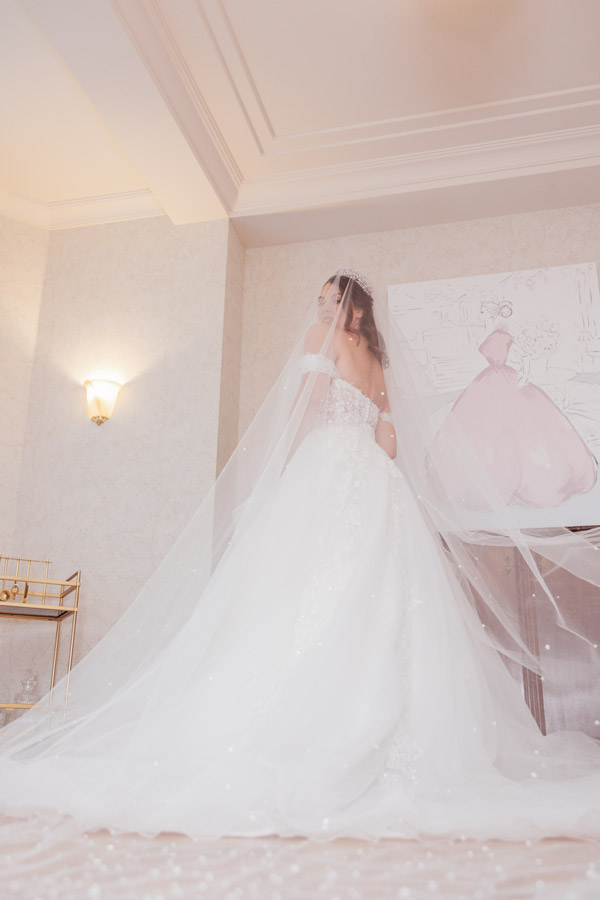 Eine Frau im weißen Brautkleid mit Schleier steht lächelnd in elegantem Zimmer