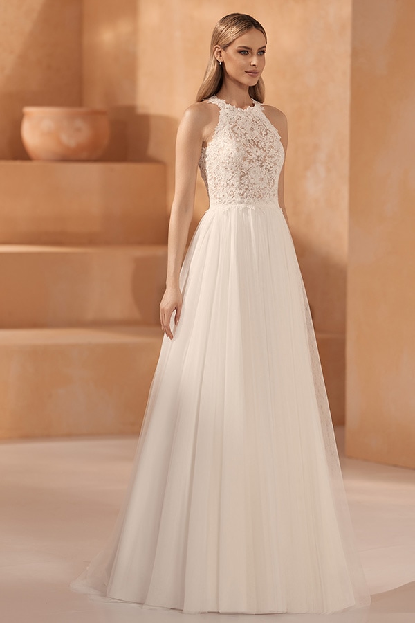 Junge Frau mit langen blonden Haaren trägt ein cremeweißes Brautkleid und lächelt leicht