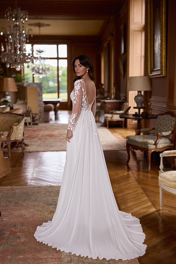 Eine brünette Frau blickt ruhig zurück, trägt ein elegantes weißes Brautkleid mit Spitze