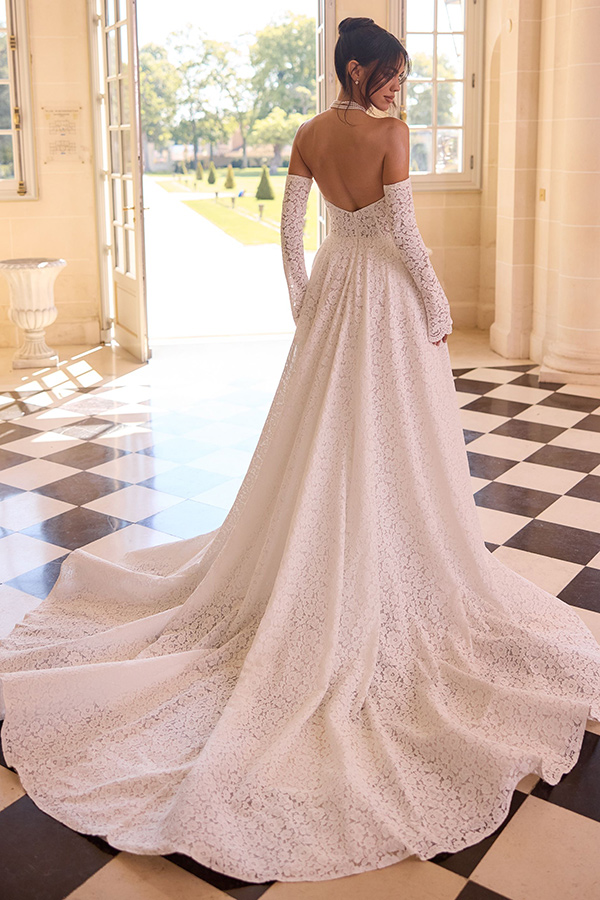 Eine Frau in elegantem weißen Spitzenkleid mit offener Schulter steht auf schwarzweißem Schachbrettboden