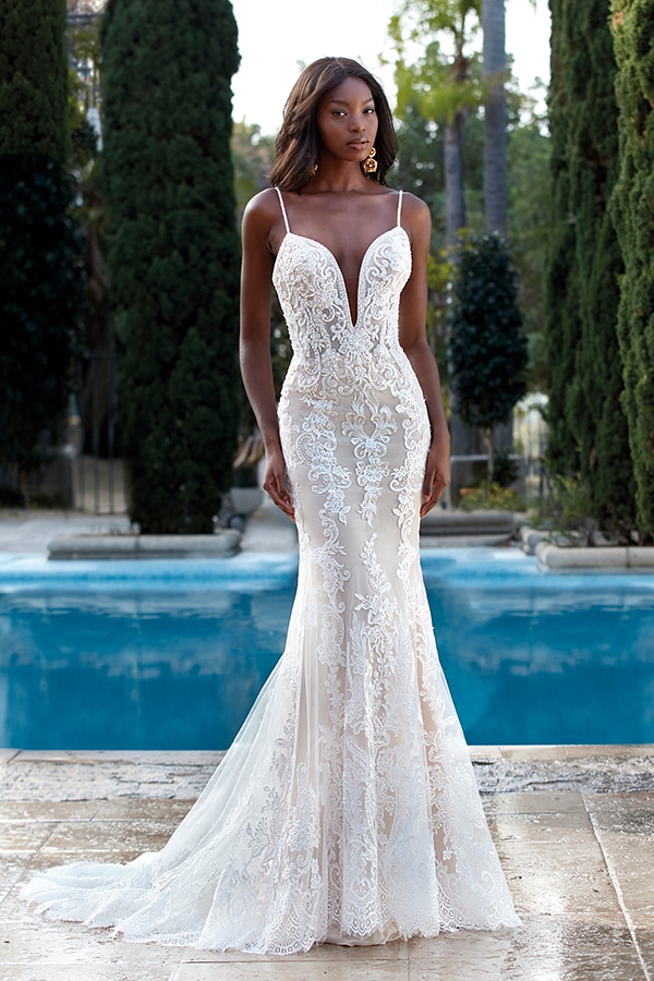 Eine elegante Frau mit ernster Miene trägt ein elfenbeinfarbenes Spitzenkleid am Pool