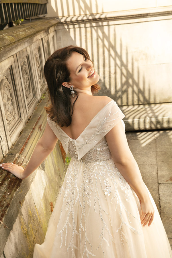 Eine Frau mit dunklem Haar lächelt strahlend in einem cremefarbenen Glitzerkleid