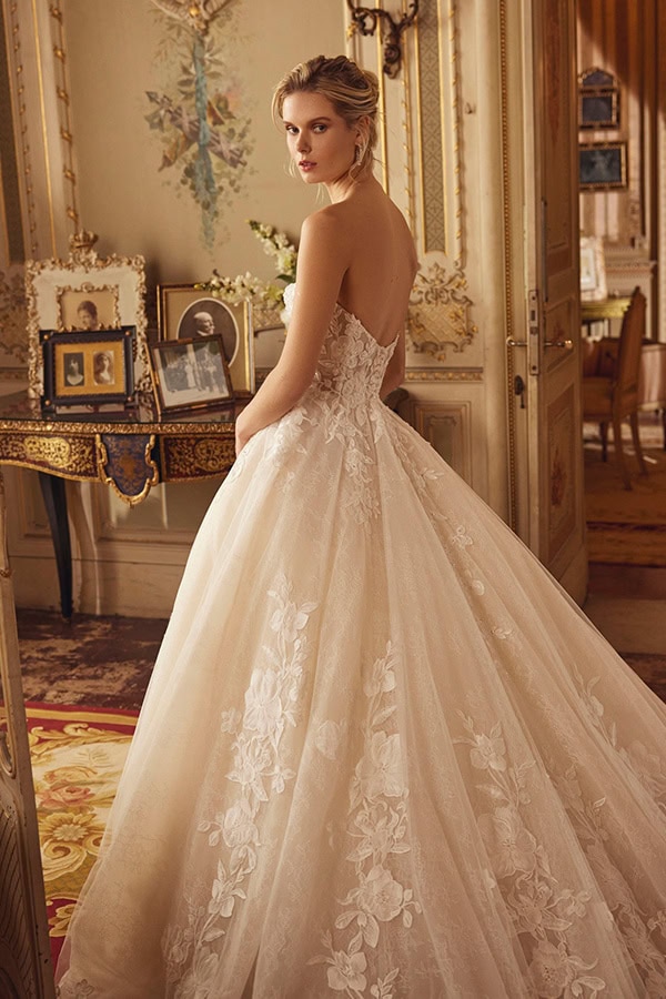 Eine blonde Frau in einem eleganten cremefarbenen Brautkleid blickt ernst zurück