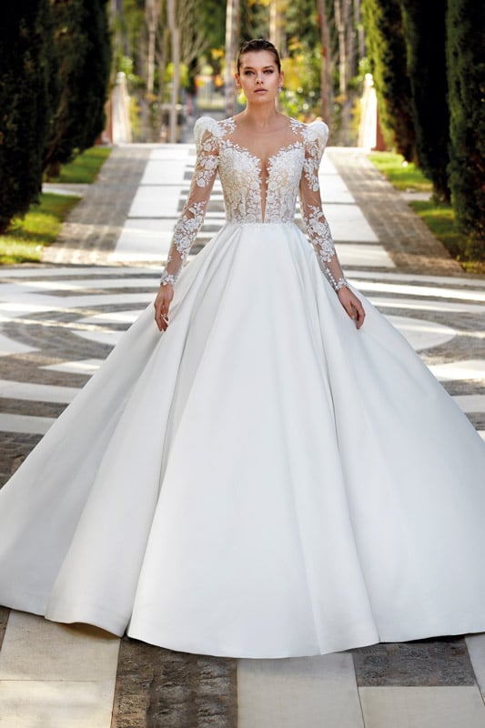 Eine junge Frau mit neutralem Gesichtsausdruck trägt ein elegantes weißes Brautkleid
