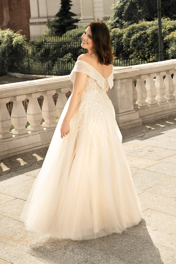 Junge lächelnde Frau in cremefarbenem Brautkleid steht draußen auf einem Steinweg